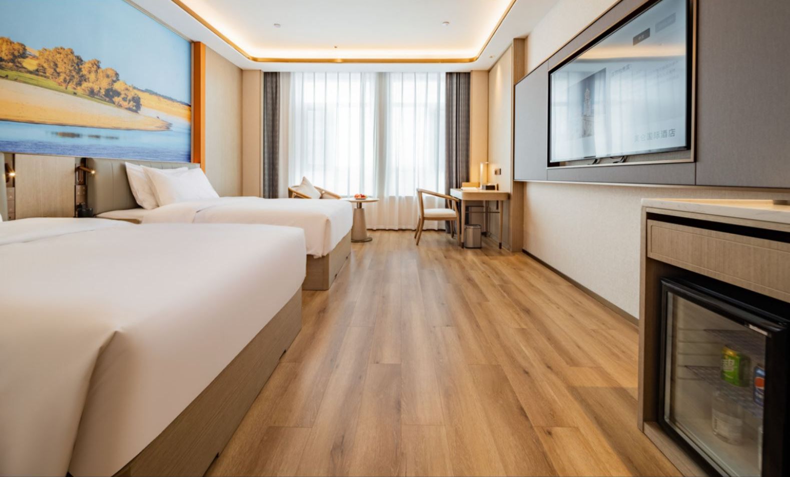 A hotel room with two beds, a desk, a chair, a television, and a minibar.