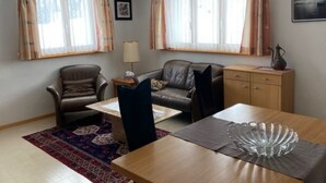 Ett rum med en soffa, en fåtölj, ett litet bord, ett skåp och ett fönster med gardiner.