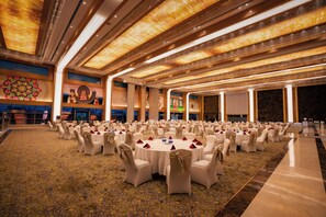 A large banquet hall with round tables, white chairs, and a patterned carpet.