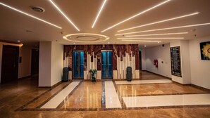 A spacious lobby with a polished marble floor, a central column, and a modern ceiling design with linear lighting. - Aureum Grand Hotels & Resorts (Pathankot)