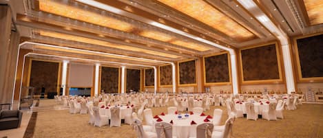 Un amplio salón de banquetes con filas de mesas redondas, cada una con sillas blancas y servilletas rojas.