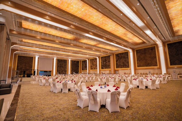 Un amplio salón de banquetes con filas de mesas redondas, cada una con sillas blancas y servilletas rojas.