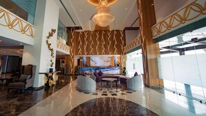 A spacious lobby with a large chandelier, seating area, and a large window. - Aureum Grand Hotels & Resorts (Pathankot)