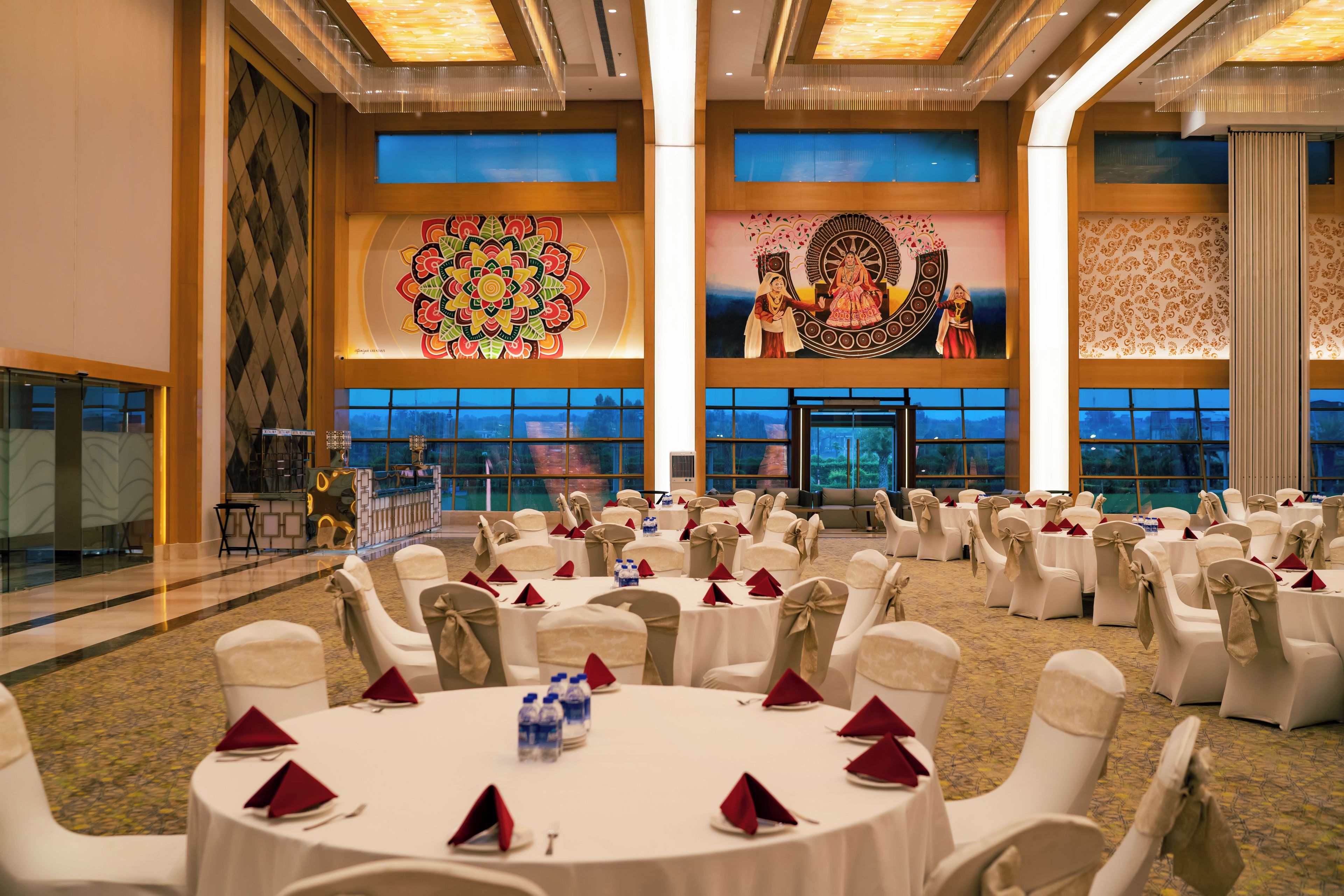 A banquet hall with round tables, white chairs, and red napkins.