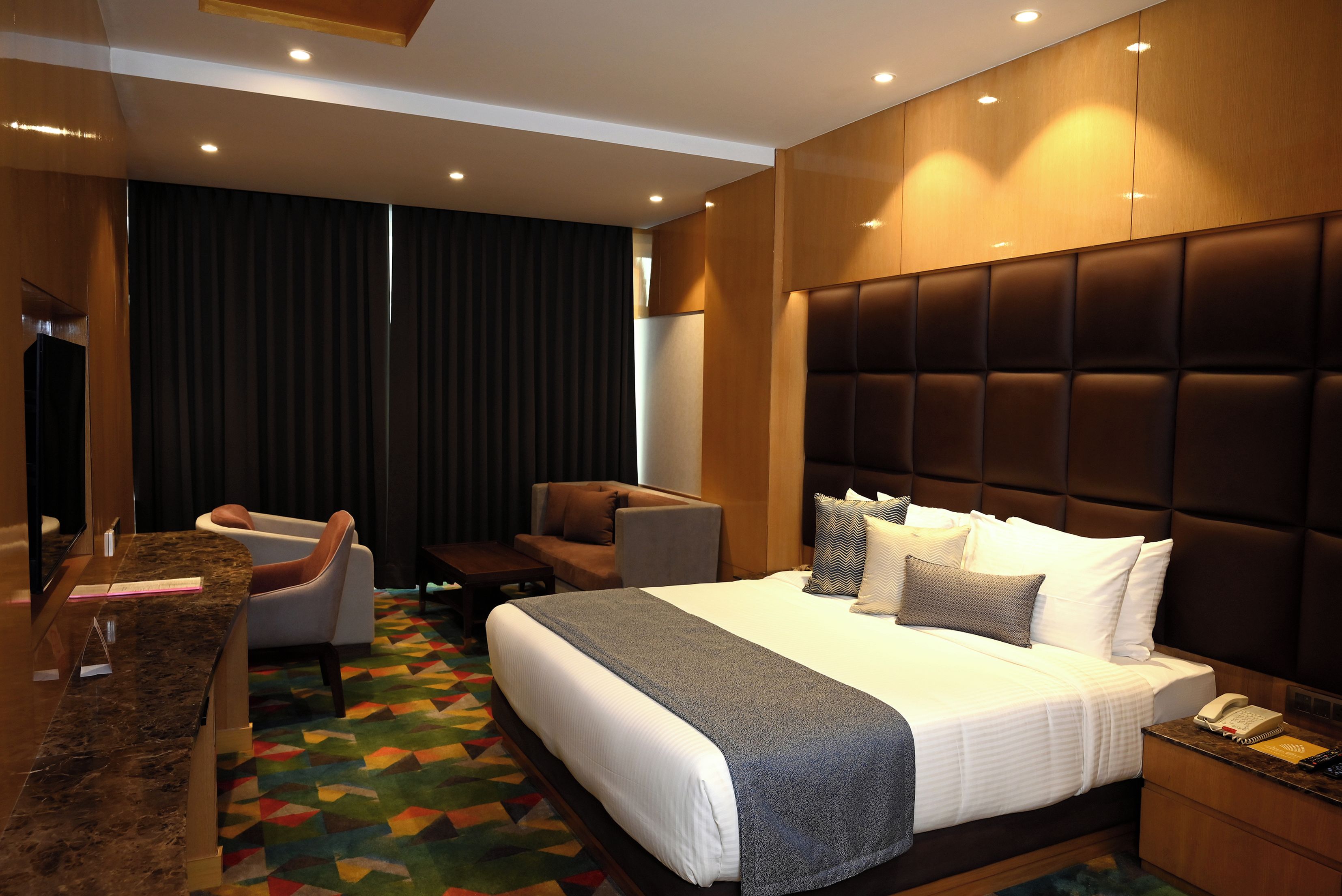 Ein modernes Hotelzimmer mit einem großen Bett, einer Sitzecke mit Stühlen, einem Schreibtisch und einem Fernseher.