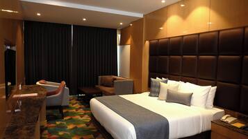 Ein modernes Hotelzimmer mit einem großen Bett, einer Sitzecke mit Stühlen, einem Schreibtisch und einem Fernseher.