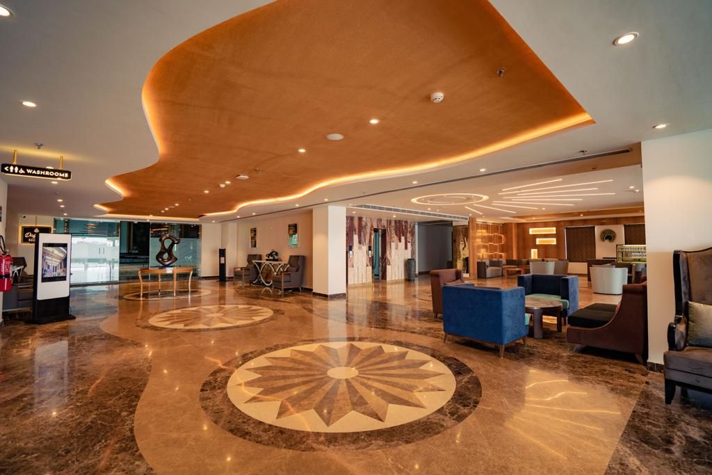 Eine großzügige Lobby mit modernem Design, ausgestattet mit einer zentralen Sitzecke, einem Empfangsschalter und einem freien Zugang zur Eingangstür.