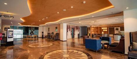 A spacious lobby with a modern design, featuring a central seating area, a reception desk, and a clear path leading to the entrance.