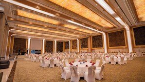 A large banquet hall with rows of round tables, each set with white chairs and red napkins. - Aureum Grand Hotels & Resorts (Pathankot)
