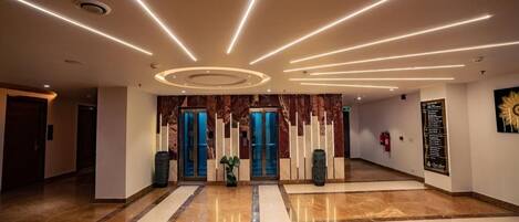 Un lobby espacioso con piso de mármol pulido, una columna central y un diseño de techo moderno con iluminación lineal.