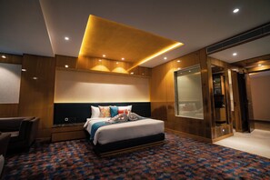 Une chambre d’hôtel moderne dotée d’un grand lit, d’un coin salon et d’une salle de bain entièrement vitrée.