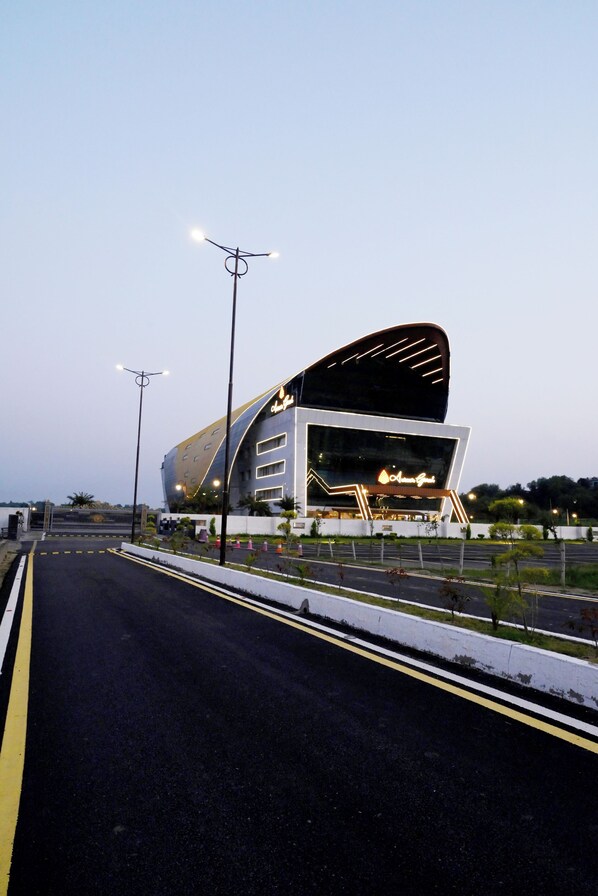 Un edificio moderno con fachada curva, una entrada iluminada grande y un camino de acceso con puerta.