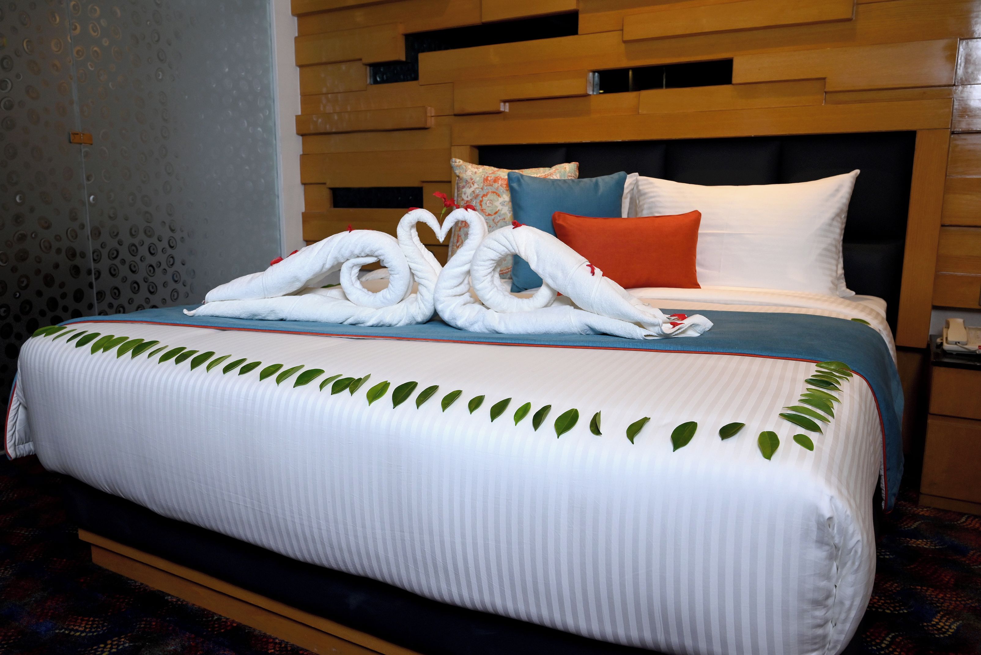 Une chambre d’hôtel avec un lit agrémenté d’une décoration en forme de cœur réalisée avec des serviettes, un mur à motifs et une tête de lit en bois.
