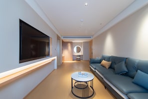 A modern hotel room with a large flat-screen TV mounted on the wall, a sofa, a round coffee table, and a circular mirror on the wall. - Ji Hotel Changchun Silicon Valley Street Party Sch (Changchun)