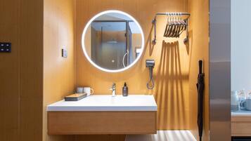 A modern bathroom with a wooden vanity, a round mirror, a handheld showerhead, and a towel rack.