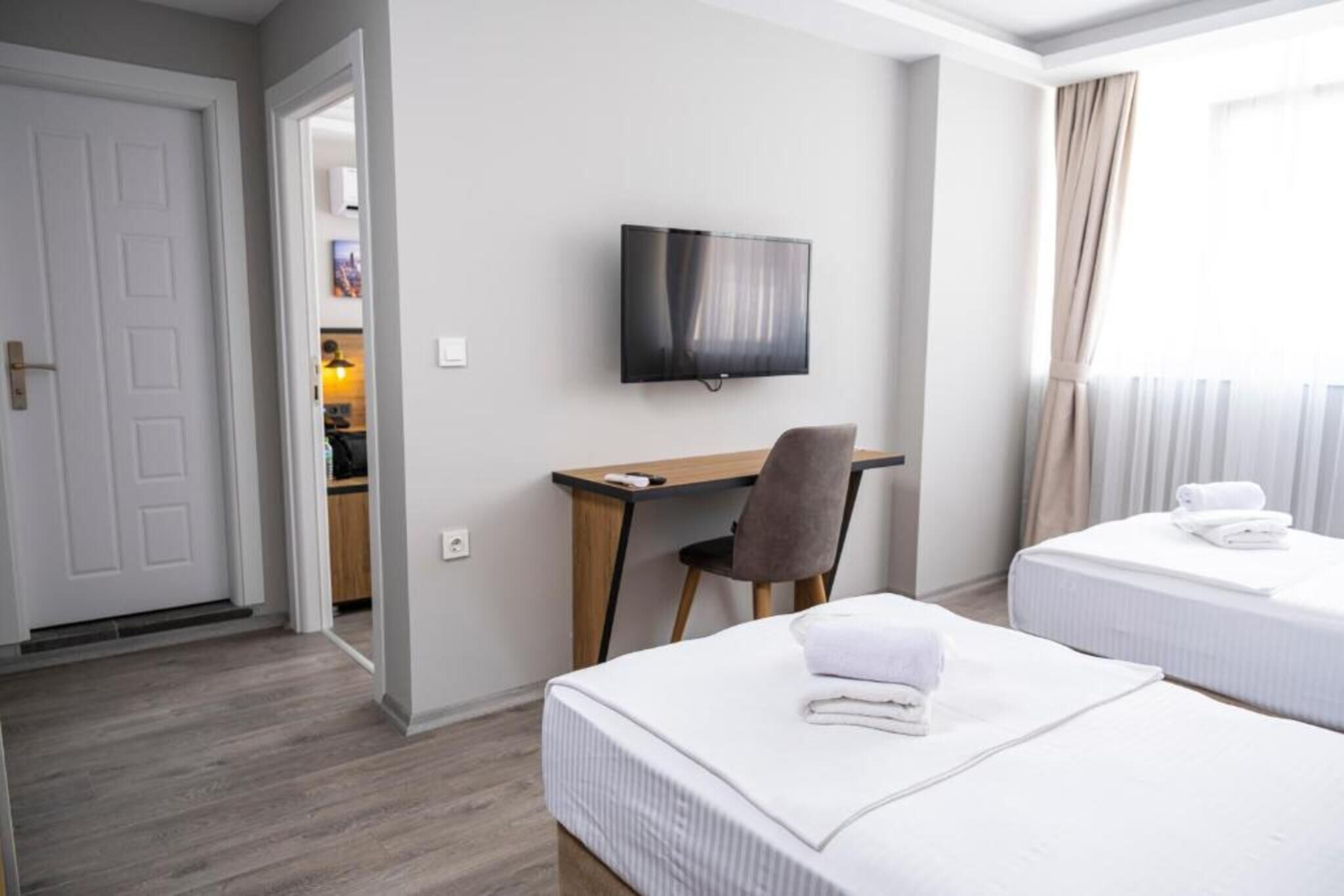 A hotel room with two beds, a desk, a chair, a television, and a door leading to another room.