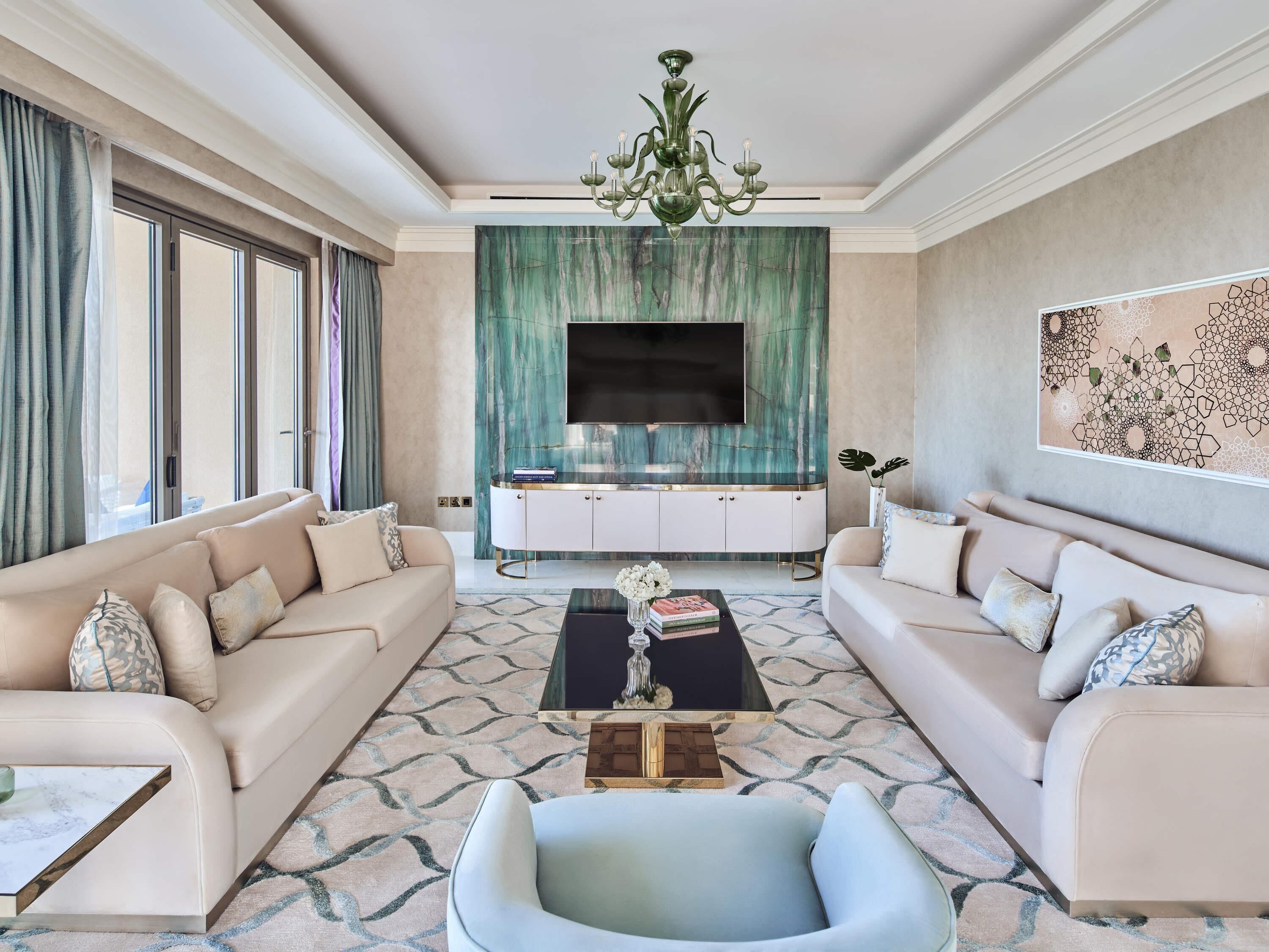 A spacious living room with a large TV, two sofas, a coffee table, and a chandelier.