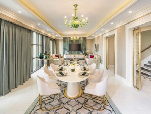 A dining room with a round table, white chairs, a chandelier, and a TV in the background. - Club Prive By Rixos Saadiyat (Abu Dhabi)