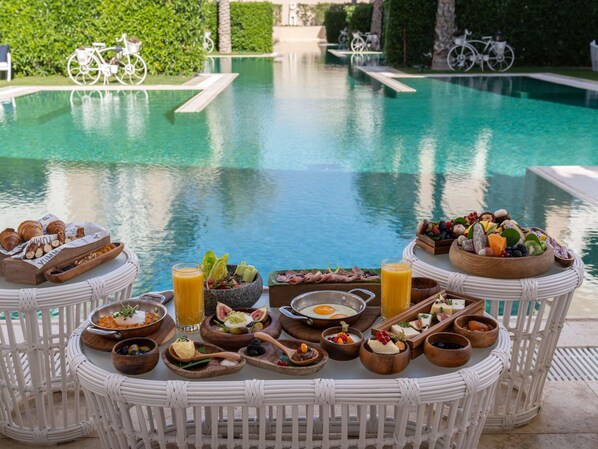 A breakfast buffet with various foods and drinks by a poolside. - Club Prive By Rixos Saadiyat (Abu Dhabi)