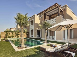 A modern two-story building with a swimming pool, outdoor seating, and palm trees.