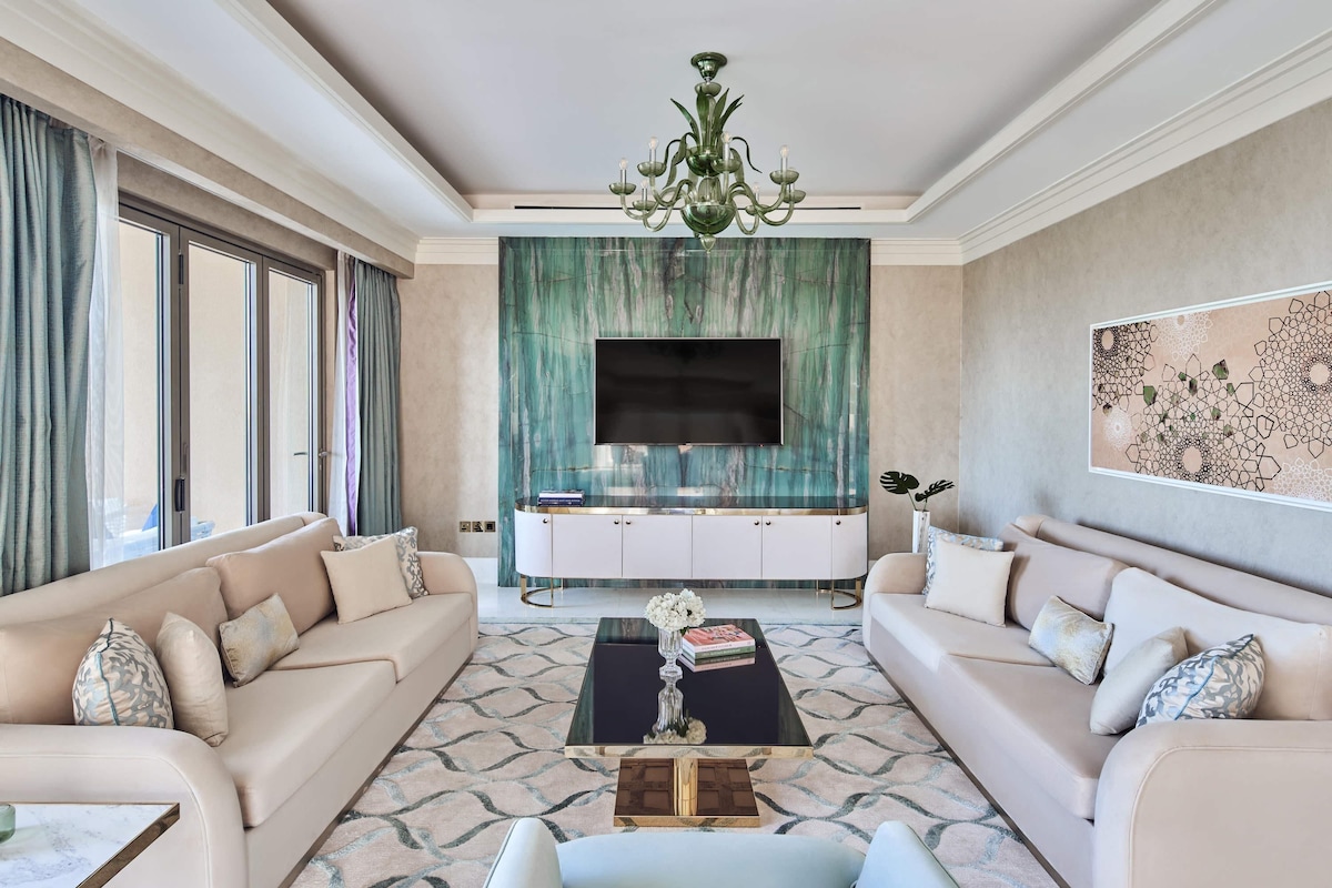 A spacious living room with a large TV, two sofas, a coffee table, and a chandelier.