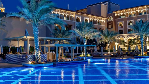 A hotel with a large swimming pool, palm trees, and a building with arches and a tower. - Club Prive By Rixos Saadiyat (Abu Dhabi)