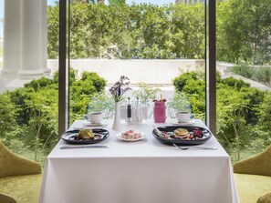 A table set for a meal with a view of a manicured garden and a pathway.