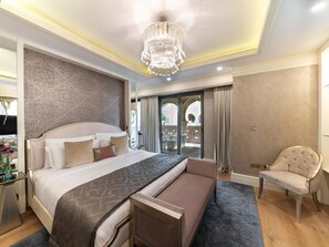 A spacious bedroom with a large bed, a chandelier, a balcony with a view, and a seating area.
