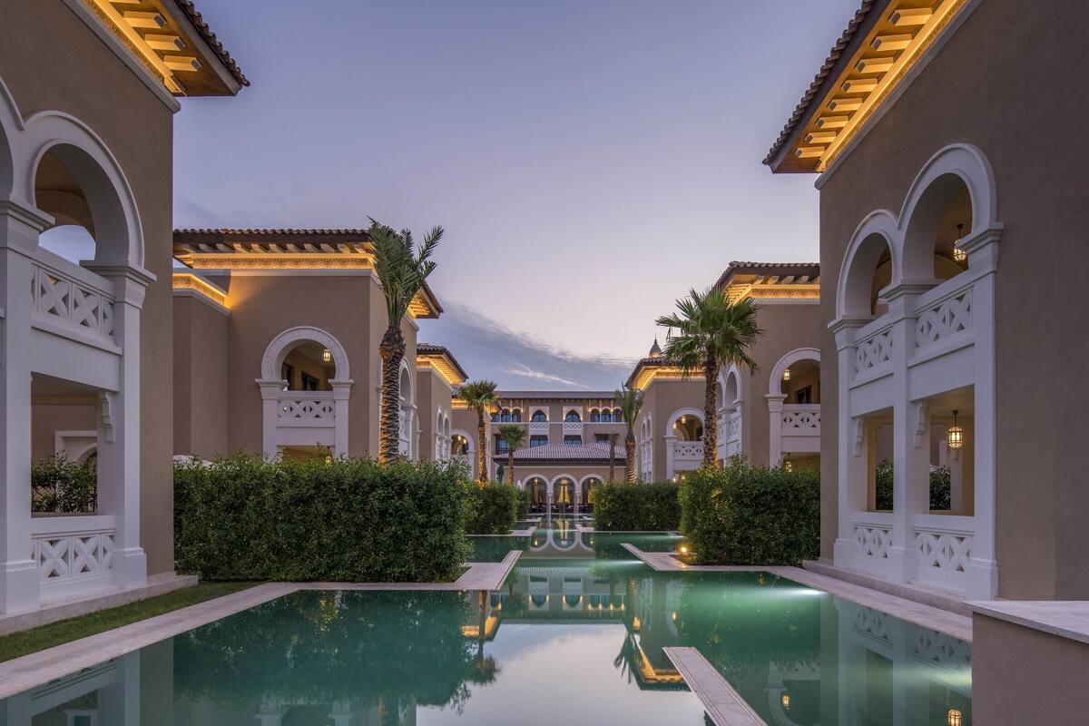 A pool area with a reflection, surrounded by buildings with arches and columns.