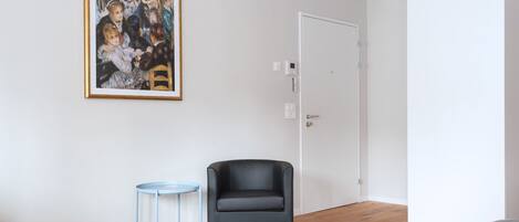 Una habitación con una cama, una silla, una mesita, una puerta y un cuadro enmarcado en la pared.