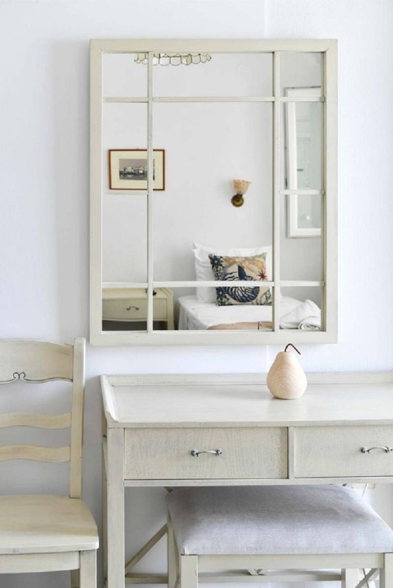 Une commode blanche avec des tiroirs, un miroir et un vase.
