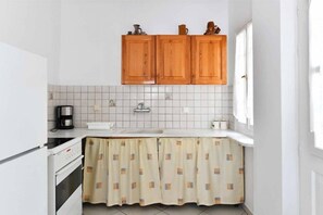 A small kitchen with white cabinets, a tiled backsplash, a coffee maker, and a patterned curtain. - Hara Studios (Paros)