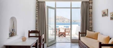 A room with a dining table, chairs, a sofa, and a view of the sea through a glass door.