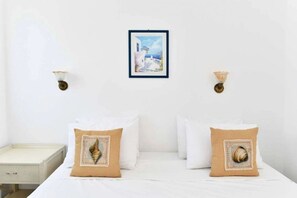 A bedroom with a bed, two pillows, a nightstand, and a framed picture on the wall. - Hara Studios (Paros)