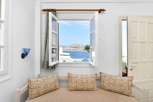 Una habitación con ventana saliente, una cama con almohadillas estampadas y vistas a un paisaje costero.