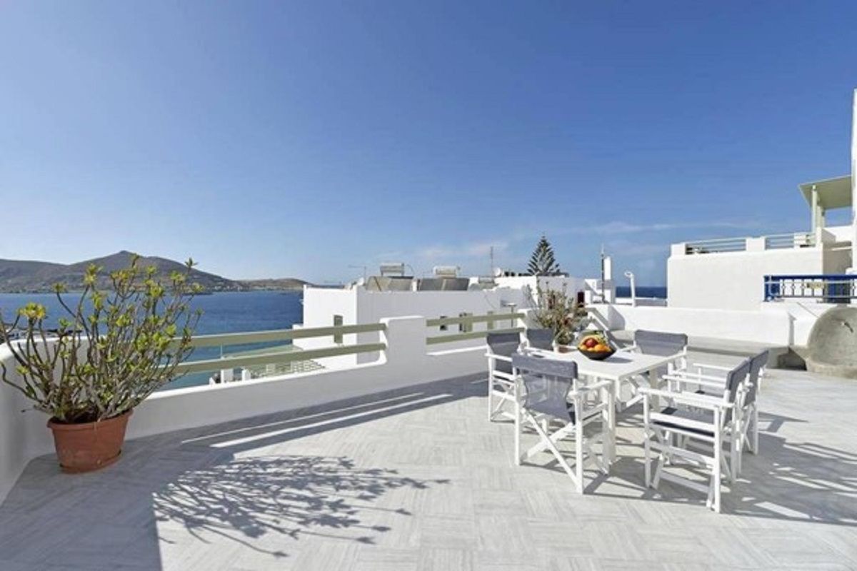 A terrace with white furniture, a potted plant, and a view of the sea.