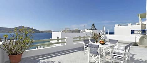 A terrace with white furniture, a potted plant, and a view of the sea.