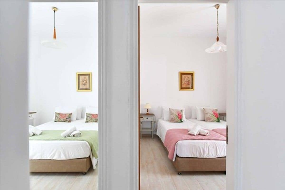 Two identical bedrooms with white walls, a bed with a green and pink bedspread, a bedside table with a lamp, and a framed picture on the wall.