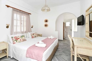 A hotel room with a bed, a desk, a television, and a chandelier. - Hara Studios (Paros)