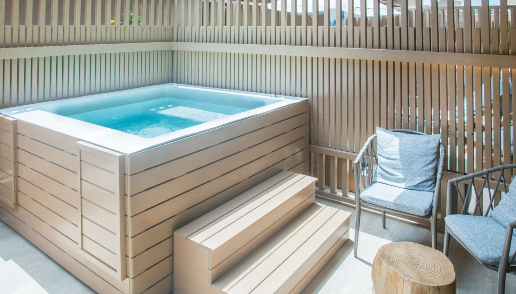 A hot tub with wooden steps and a chair with a cushion.