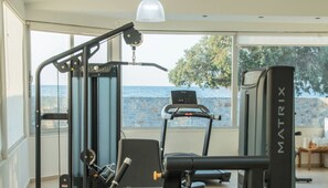 A gym with exercise equipment, a treadmill, and a view of the sea through large windows. - Senseana Seaside Resort And Aquadventure (Analipsis)
