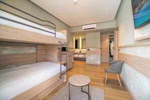 A modern hotel room with bunk beds, a small round table, a chair, a bathroom with a mirror, and a TV on the wall. - Senseana Seaside Resort And Aquadventure (Analipsis)