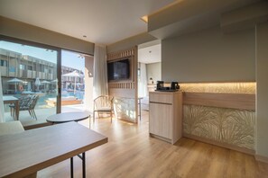 A modern hotel room with a dining area, a TV mounted on the wall, and a view of the pool outside. - Senseana Seaside Resort And Aquadventure (Analipsis)