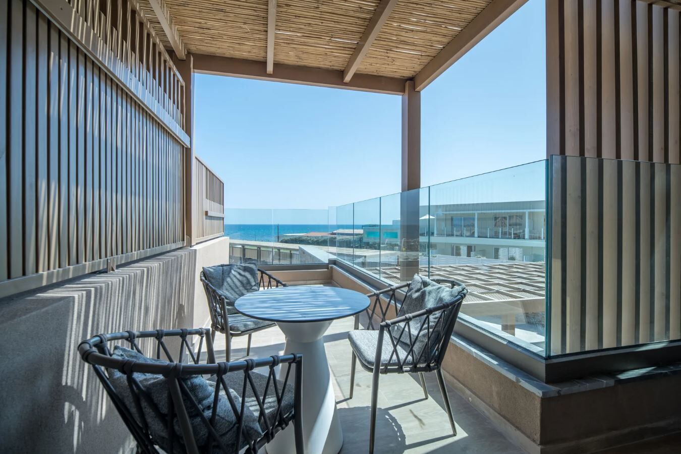 A balcony with a glass railing, two chairs, a table, and a view of the sea.