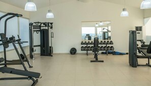 A gym with various exercise equipment, including a bench press, weight machines, and dumbbells. - Senseana Seaside Resort And Aquadventure (Analipsis)