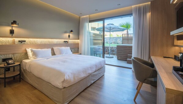 A modern hotel room with a large bed, a desk, and a balcony with outdoor furniture. - Senseana Seaside Resort And Aquadventure (Analipsis)