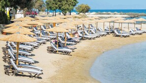 A beach with rows of sun loungers and thatched umbrellas, a clear sky, and a calm sea. - Senseana Seaside Resort And Aquadventure (Analipsis)