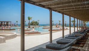 Zona junto a la piscina con sillones reclinables, terraza solárium y vista al océano.