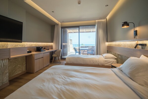 A hotel room with two beds, a desk, a flat-screen TV, and a view of the sea. - Senseana Seaside Resort And Aquadventure (Analipsis)