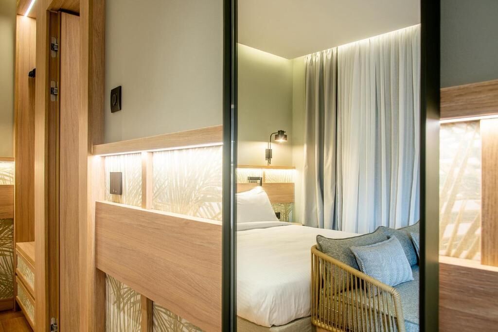A hotel room with a bed, a bedside table, a lamp, and a window with curtains.